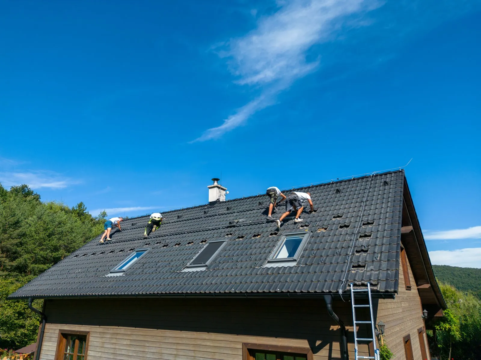 Twee dakdekkers aan het werk op een donker pannendak onder een blauwe lucht